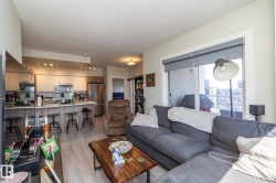 Open-concept living area featuring a modern kitchen with light cabinetry, stainless steel appliances, and a breakfast bar - 