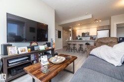 Open-concept living area featuring light wood-finish flooring, a contemporary kitchen with stainless steel appliances, a spacious island with bar seating, and recessed lighting - 