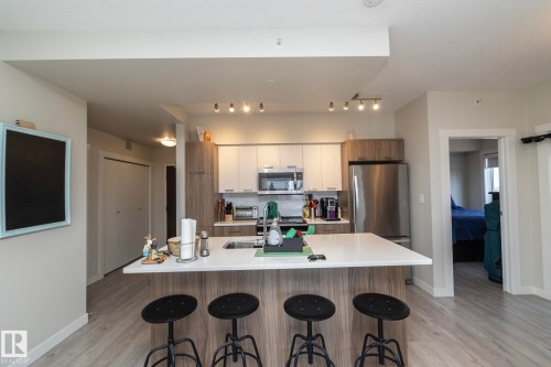 Modern kitchen featuring an island with seating, stainless steel appliances, contemporary cabinetry, a built-in microwave, and track lighting - #2402 10410 102 Av Nw, Edmonton, AB - Indoor Photo Showing Kitchen With Stainless Steel Kitchen With Upgraded Kitchen