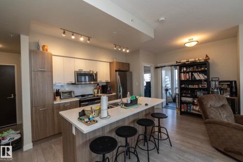 Open-concept kitchen featuring an island with seating, stainless steel appliances, two-tone cabinetry, and wood-finish flooring - #2402 10410 102 Av Nw, Edmonton, AB - Indoor Photo Showing Kitchen With Stainless Steel Kitchen