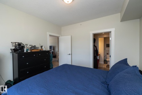 Spacious bedroom featuring a blue upholstered bed, black dresser with multiple drawers, ceiling-mounted light fixture, and direct access to multiple closets and adjoining rooms through white-trimmed doorways - #2402 10410 102 Av Nw, Edmonton, AB - Indoor Photo Showing Bedroom