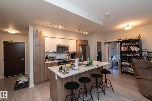 Modern kitchen featuring two-tone cabinetry, stainless steel appliances, a white countertop island, and wood-finish flooring - #2402 10410 102 Av Nw, Edmonton, AB - Indoor Photo Showing Kitchen
