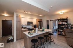Modern kitchen featuring two-tone cabinetry, stainless steel appliances, a white countertop island, and wood-finish flooring - 