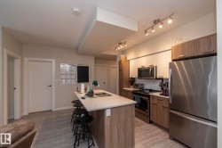 Modern kitchen with a light wood-finish island and white countertop, stainless steel appliances, and track lighting - 