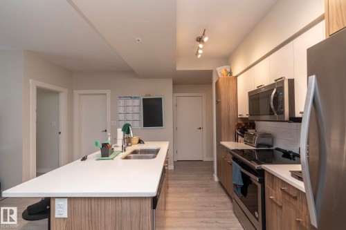 Modern kitchen featuring a large island with an undermount sink, white countertops, stainless steel appliances, and two-tone cabinetry - #2402 10410 102 Av Nw, Edmonton, AB - Indoor Photo Showing Kitchen With Stainless Steel Kitchen With Double Sink