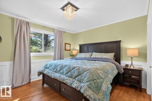 Hardwood flooring throughout featuring white board and batten wall paneling, a large window with natural light, and a crystal chandelier - 4631 113A Street Nw, Edmonton, AB - Indoor Photo Showing Bedroom