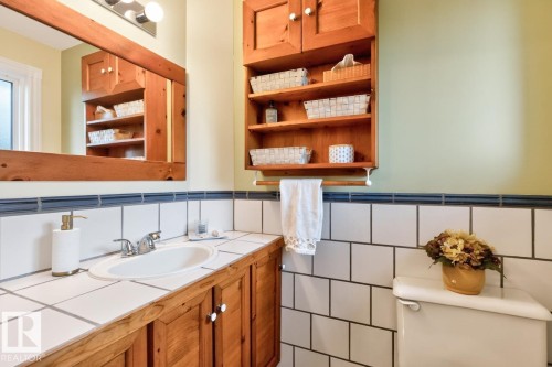 Bathroom featuring a wooden vanity with a white tile countertop, an oval undermount sink, and a chrome faucet - 4631 113A Street Nw, Edmonton, AB - Indoor Photo Showing Bathroom