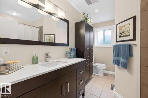 Bathroom featuring a dark wood-finish vanity with a white countertop and undermount sink, a large framed mirror, and a multi-bulb light fixture - 4631 113A Street Nw, Edmonton, AB - Indoor Photo Showing Bathroom
