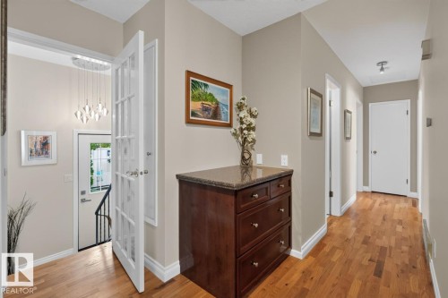 Hardwood flooring throughout a hallway featuring neutral wall tones, white trim, and a built-in dark wood cabinet with a stone countertop - 4631 113A Street Nw, Edmonton, AB - Indoor Photo Showing Other Room