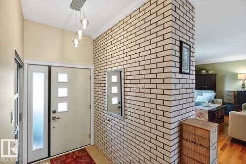 Entryway featuring a modern front door with frosted glass panels and a sidelight, a contemporary hanging light fixture, and an accent wall with brick-look tile - 4631 113A Street Nw, Edmonton, AB - Indoor Photo Showing Other Room