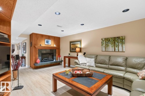 Living area featuring light wood-finish flooring and a fireplace with a stone surround and wood mantelpiece - 4631 113A Street Nw, Edmonton, AB - Indoor Photo Showing Living Room With Fireplace