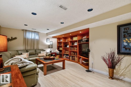 Spacious living area featuring light wood-finish flooring, recessed lighting, and a built-in wood shelving unit - 4631 113A Street Nw, Edmonton, AB - Indoor
