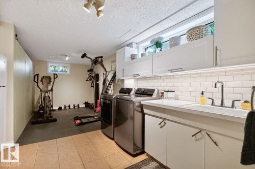 Spacious utility area featuring a laundry sink, white shaker-style cabinetry, and a subway tile backsplash - 4631 113A Street Nw, Edmonton, AB - Indoor Photo Showing Laundry Room