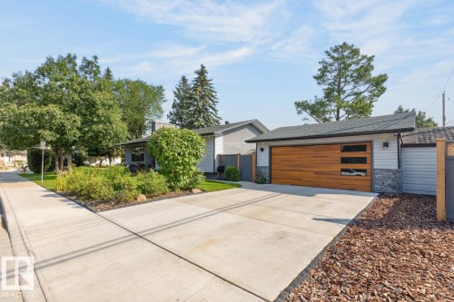 Contemporary exterior featuring a wood-finish garage door with horizontal windows, light-colored siding, and stone accents - 4631 113A Street Nw, Edmonton, AB - Outdoor