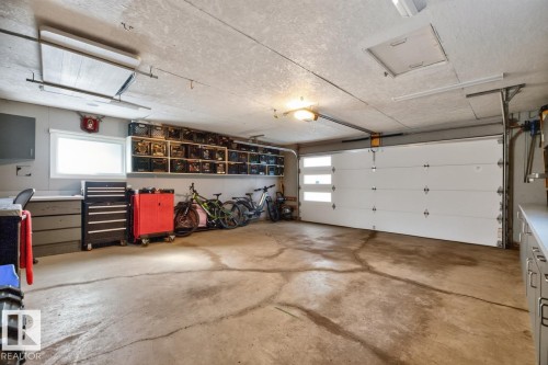 Attached garage featuring a white sectional door with horizontal window panes, overhead lighting, and built-in shelving - 4631 113A Street Nw, Edmonton, AB - Indoor Photo Showing Garage