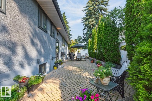 Expansive paver patio with a herringbone pattern, bordered by mature evergreen shrubs and trees - 4631 113A Street Nw, Edmonton, AB - Outdoor With Deck Patio Veranda