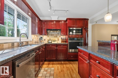 Kitchen featuring cherry-stained cabinetry, granite countertops, and stainless steel appliances including a built-in microwave, wall oven, and dishwasher - 4631 113A Street Nw, Edmonton, AB - Indoor Photo Showing Kitchen With Double Sink