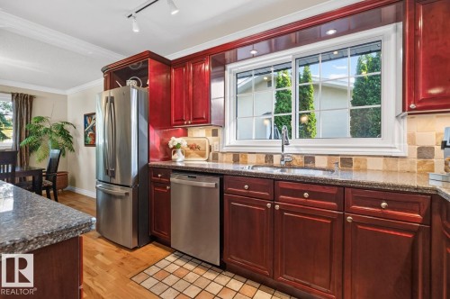 Kitchen featuring wood-finish cabinetry, stainless steel appliances, granite countertops, tile backsplash, and a window above the sink - 4631 113A Street Nw, Edmonton, AB - Indoor Photo Showing Kitchen With Stainless Steel Kitchen