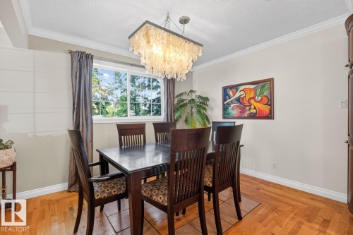 Dining area featuring wood-finish flooring with a central tiled inlay, a window with exterior tree views, and an overhead decorative chandelier - 4631 113A Street Nw, Edmonton, AB - Indoor Photo Showing Dining Room