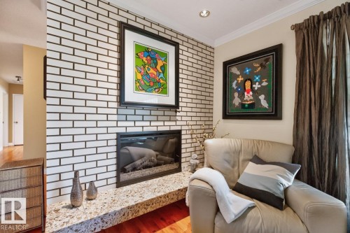 Fireplace with white brick surround and a speckled stone hearth - 4631 113A Street Nw, Edmonton, AB - Indoor Photo Showing Other Room With Fireplace