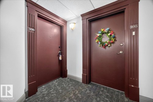 Entryway featuring two solid core doors with decorative trim, wall sconce lighting, and textured carpet flooring - #306 13111 140 Av Nw, Edmonton, AB - Indoor Photo Showing Other Room