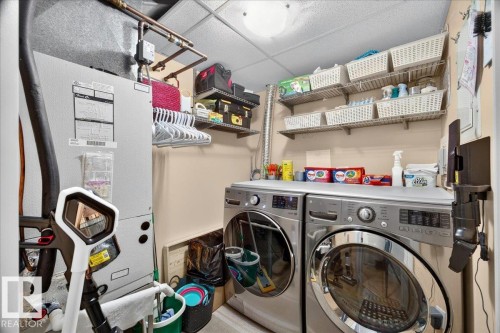 Dedicated utility space featuring a front-loading washer and dryer, an adjacent furnace unit, and overhead exposed copper piping - #306 13111 140 Av Nw, Edmonton, AB - Indoor Photo Showing Laundry Room