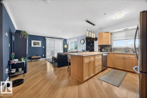 Open-concept living space featuring wood-finish flooring, a kitchen island with natural wood cabinetry, stainless steel appliances, and a glass sliding door - #306 13111 140 Av Nw, Edmonton, AB - Indoor Photo Showing Kitchen