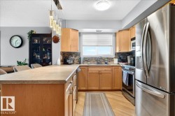 Kitchen featuring wood cabinetry, stainless steel appliances, an island with countertop seating, a mosaic tile backsplash, and wood-finish flooring - 