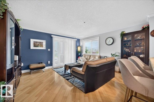 Living area featuring light wood-finish flooring, a full-height glass patio door with vertical blinds, and a window with horizontal blinds - #306 13111 140 Av Nw, Edmonton, AB - Indoor Photo Showing Living Room