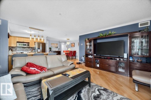Open-concept living area with wood-finish flooring, a kitchen featuring stainless steel appliances and a tile backsplash, and a dining area with pendant lighting - #306 13111 140 Av Nw, Edmonton, AB - Indoor Photo Showing Living Room