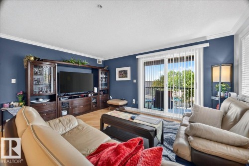 Living area featuring a sliding glass door to a private balcony, wood-finish flooring, a built-in media console, crown molding, and painted accent walls - #306 13111 140 Av Nw, Edmonton, AB - Indoor Photo Showing Living Room