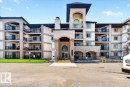 Multi-story building featuring stucco exterior, multiple balconies with black railings, a central arched entry, and a prominent tower element - #306 13111 140 Av Nw, Edmonton, AB  - Outdoor With Balcony With Facade 