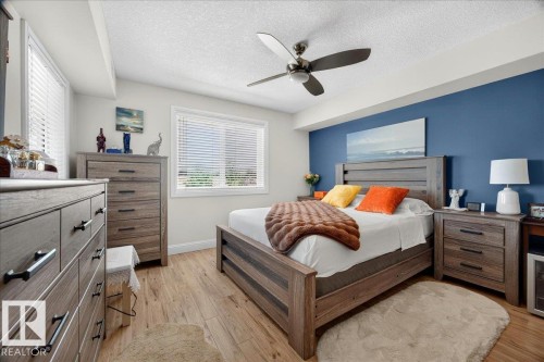 Bedroom featuring wood-finish flooring, a ceiling fan with integrated lighting, and two windows with horizontal blinds - #306 13111 140 Av Nw, Edmonton, AB - Indoor Photo Showing Bedroom