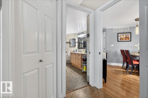 White bi-fold doors frame a hallway with wood-finish flooring - #306 13111 140 Av Nw, Edmonton, AB - Indoor Photo Showing Other Room