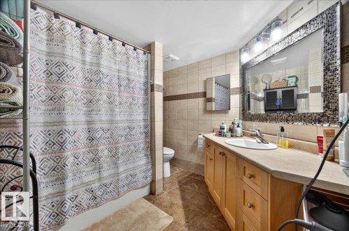 Bathroom featuring a light wood-finish vanity with a single basin sink and a large framed mirror with mosaic-style accents - #306 13111 140 Av Nw, Edmonton, AB - Indoor Photo Showing Bathroom