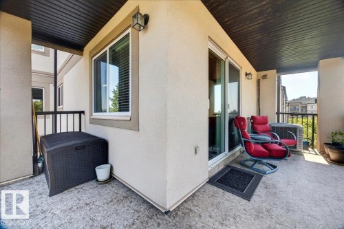 Outdoor patio featuring textured concrete flooring, black metal railings, and a dark wood soffit - #306 13111 140 Av Nw, Edmonton, AB - Outdoor With Exterior