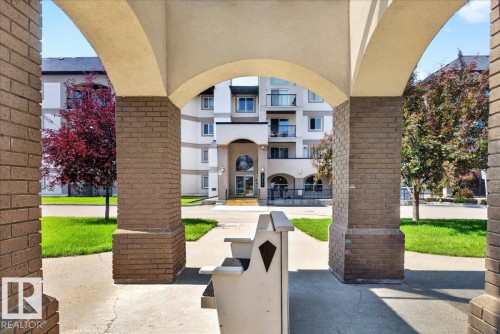 Building exterior featuring a stone facade, arched portico, glass entry doors, and individual balconies - #306 13111 140 Av Nw, Edmonton, AB - Outdoor With Balcony