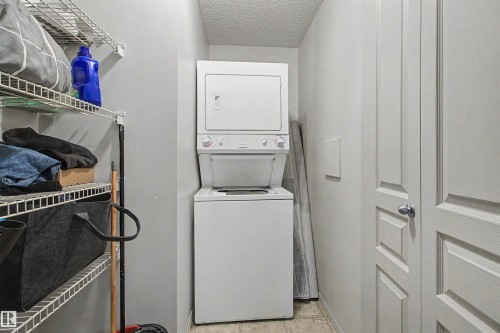 Dedicated laundry area featuring a stacked washer and dryer unit, wire shelving storage, and paneled doors - #204 309 Clareview Station Dr Nw, Edmonton, AB - Indoor Photo Showing Laundry Room