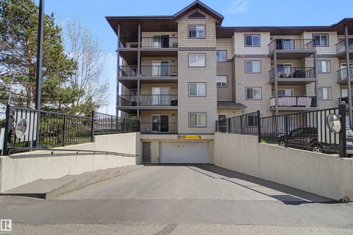 Multi-story residential building featuring a stucco and siding exterior, multiple private balconies with black railings, and a prominent sloped driveway leading to an underground parking garage - #204 309 Clareview Station Dr Nw, Edmonton, AB - Outdoor With Balcony With Facade