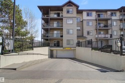 Multi-story residential building featuring a stucco and siding exterior, multiple private balconies with black railings, and a prominent sloped driveway leading to an underground parking garage - 