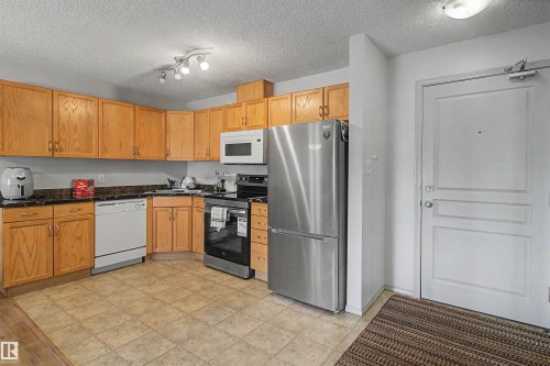 Kitchen featuring L-shaped wood cabinetry, a stainless steel refrigerator, and a built-in microwave - #204 309 Clareview Station Dr Nw, Edmonton, AB - Indoor Photo Showing Kitchen