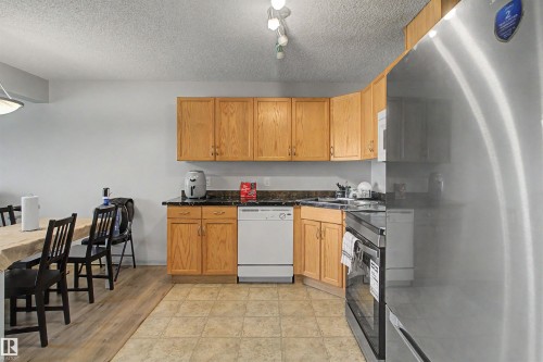Kitchen featuring wood cabinetry, dark countertops, a white dishwasher, and a stainless steel refrigerator - #204 309 Clareview Station Dr Nw, Edmonton, AB - Indoor Photo Showing Kitchen