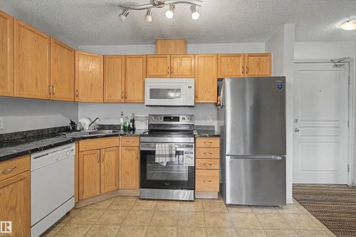 Kitchen featuring light wood cabinetry, dark countertops, and tile flooring - #204 309 Clareview Station Dr Nw, Edmonton, AB - Indoor Photo Showing Kitchen With Double Sink