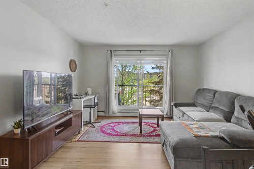 Living area featuring wood-finish flooring, light-toned walls, and a glass sliding door opening to a balcony - #204 309 Clareview Station Dr Nw, Edmonton, AB - Indoor Photo Showing Living Room