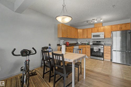 Kitchen and dining area featuring wood-finish flooring, light wood cabinetry, stainless steel appliances, and a track lighting fixture - #204 309 Clareview Station Dr Nw, Edmonton, AB - Indoor Photo Showing Other Room