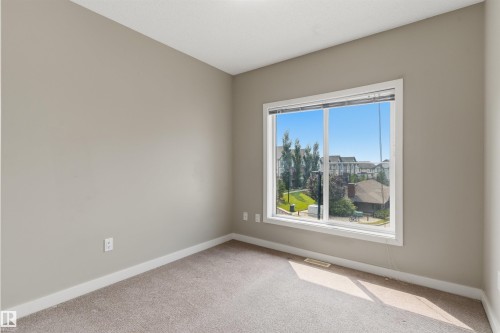 Carpeted room with neutral paint, white trim, and a large window - #62 675 Watt Bv Sw, Edmonton, AB - Indoor Photo Showing Other Room