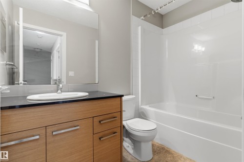 Bathroom featuring a light wood-finish vanity with a dark countertop, an undermount sink, and a large wall-mounted mirror - #62 675 Watt Bv Sw, Edmonton, AB - Indoor Photo Showing Bathroom