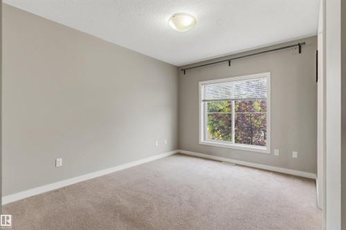 Neutral-toned room featuring a large window, light brown carpeting, and white baseboards - #62 675 Watt Bv Sw, Edmonton, AB - Indoor Photo Showing Other Room