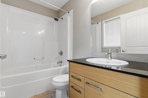 Bathroom vanity with wood-finish cabinetry, a dark countertop, and an oval undermount sink - #62 675 Watt Bv Sw, Edmonton, AB - Indoor Photo Showing Bathroom