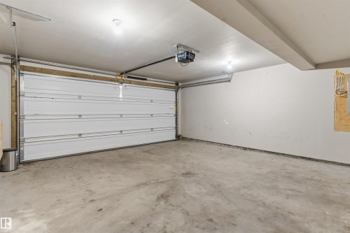 Spacious garage featuring a concrete floor, white sectional garage door, and an automatic garage door opener - #62 675 Watt Bv Sw, Edmonton, AB - Indoor Photo Showing Garage